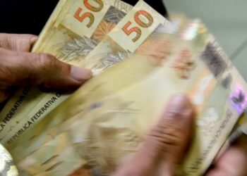 Mãos segurando notas de dinheiro em real, representando o Crédito Caixa Tem de até R$ 1000 em 2025