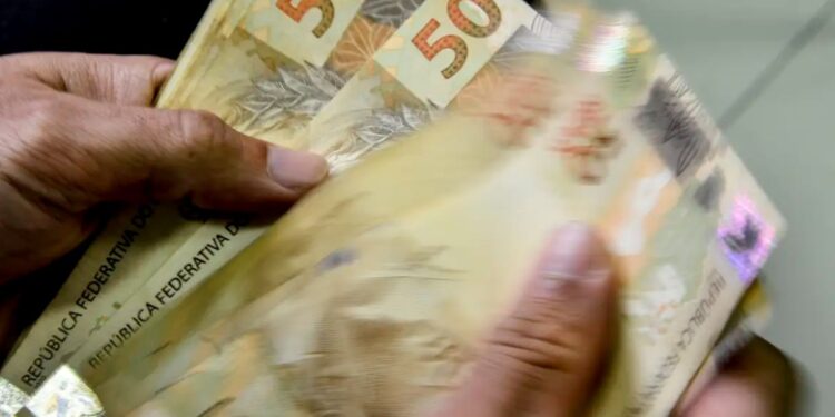 Mãos segurando notas de dinheiro em real, representando o Crédito Caixa Tem de até R$ 1000 em 2025