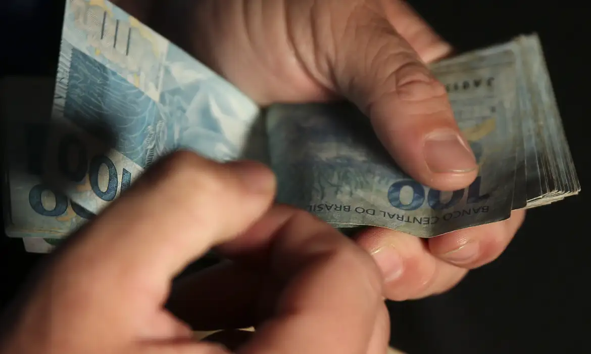 pessoa contando notas de cem reais em ambiente fechado