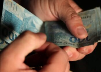 Pessoa contando notas de 100 reais em ambiente fechado