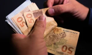 Pessoa contando cédulas de cinquenta reais, simbolizando reajustes no salário mínimo no Brasil