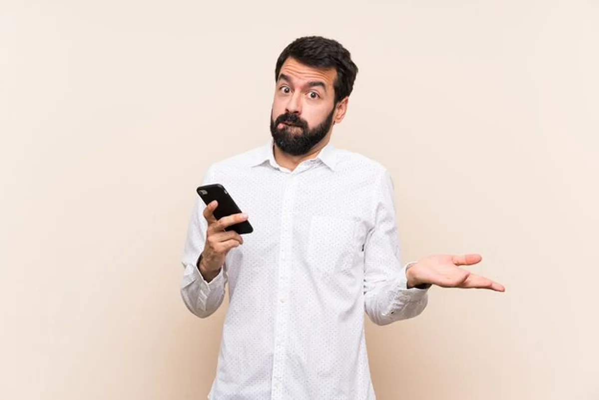 Homem em dúvida com o celular na mão, representando quem consultou e não entende por que a restituição do IR 2026 ainda não caiu na conta