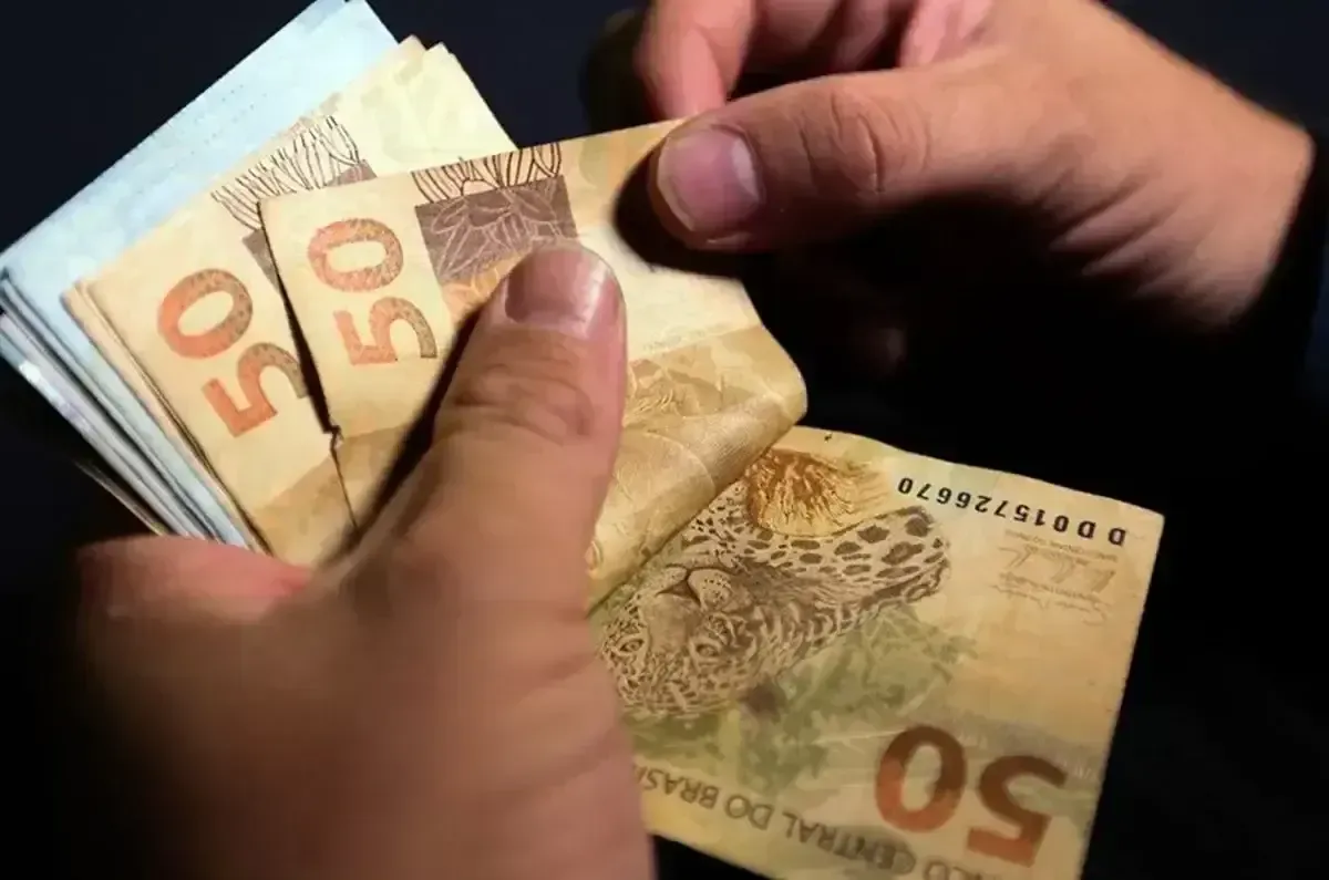 Pessoa contando notas de 50 reais, simbolizando o pagamento do reajuste do dissídio de 2025.