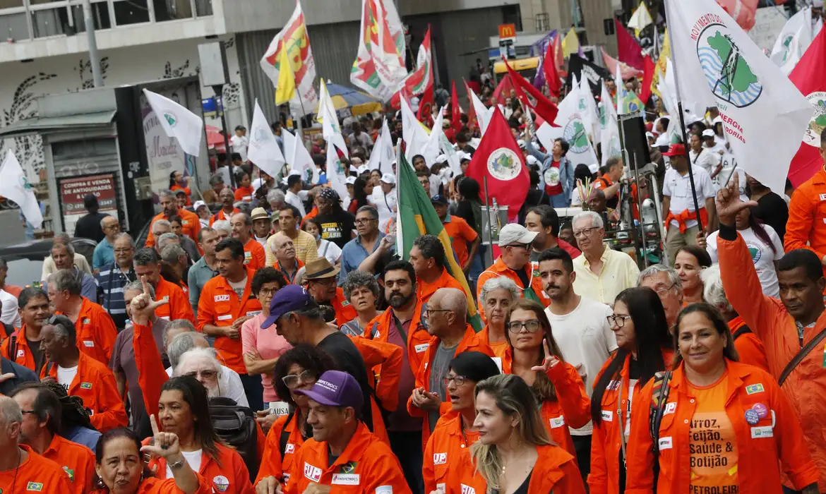 "Manifestação de trabalhadores com bandeiras, reforçando a importância da negociação coletiva para o trabalho aos domingos e feriados."