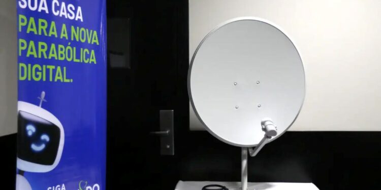 Kit gratuito da nova parabólica digital com antena e acessórios em uma bancada, ao lado de banner explicativo.
