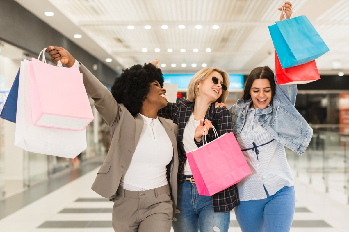 Mulheres felizes saindo de shopping cheias de sacolas, representando a movimentação do comércio com a antecipação do salário.