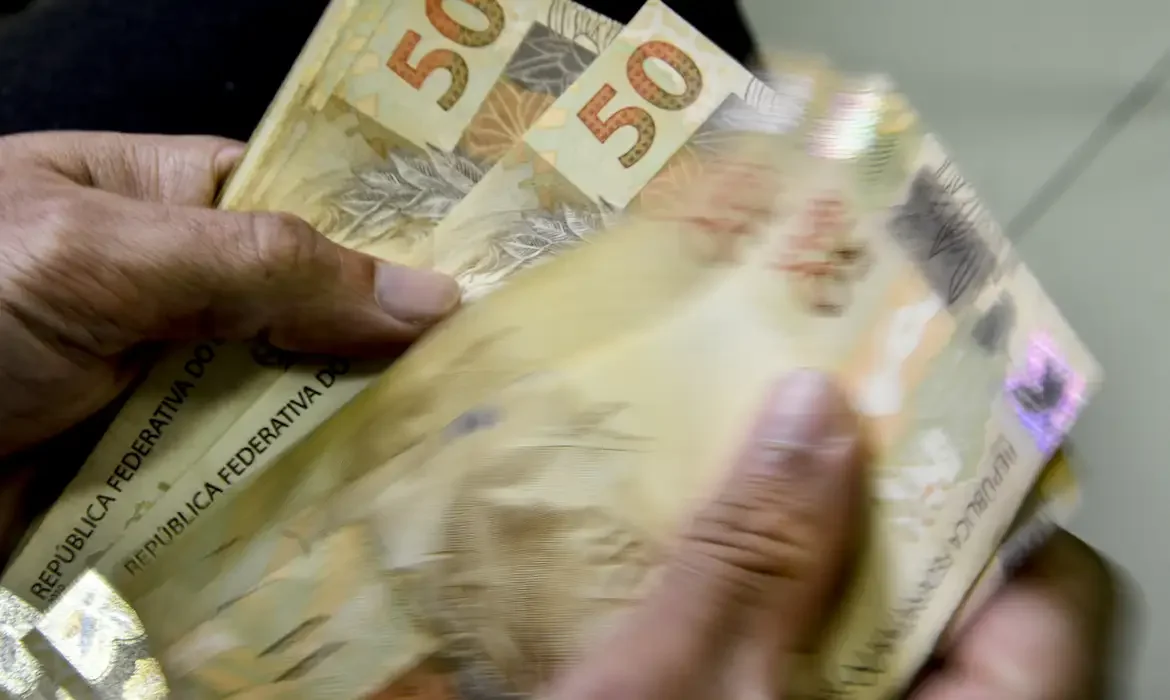 "Pessoa segurando várias cédulas de 50 reais, representando a importância de atender aos requisitos para o abono salarial."