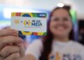 Jovem sorridente segura cartão "Pé-de-Meia" com frase "A poupança do ensino médio", fundo colorido
