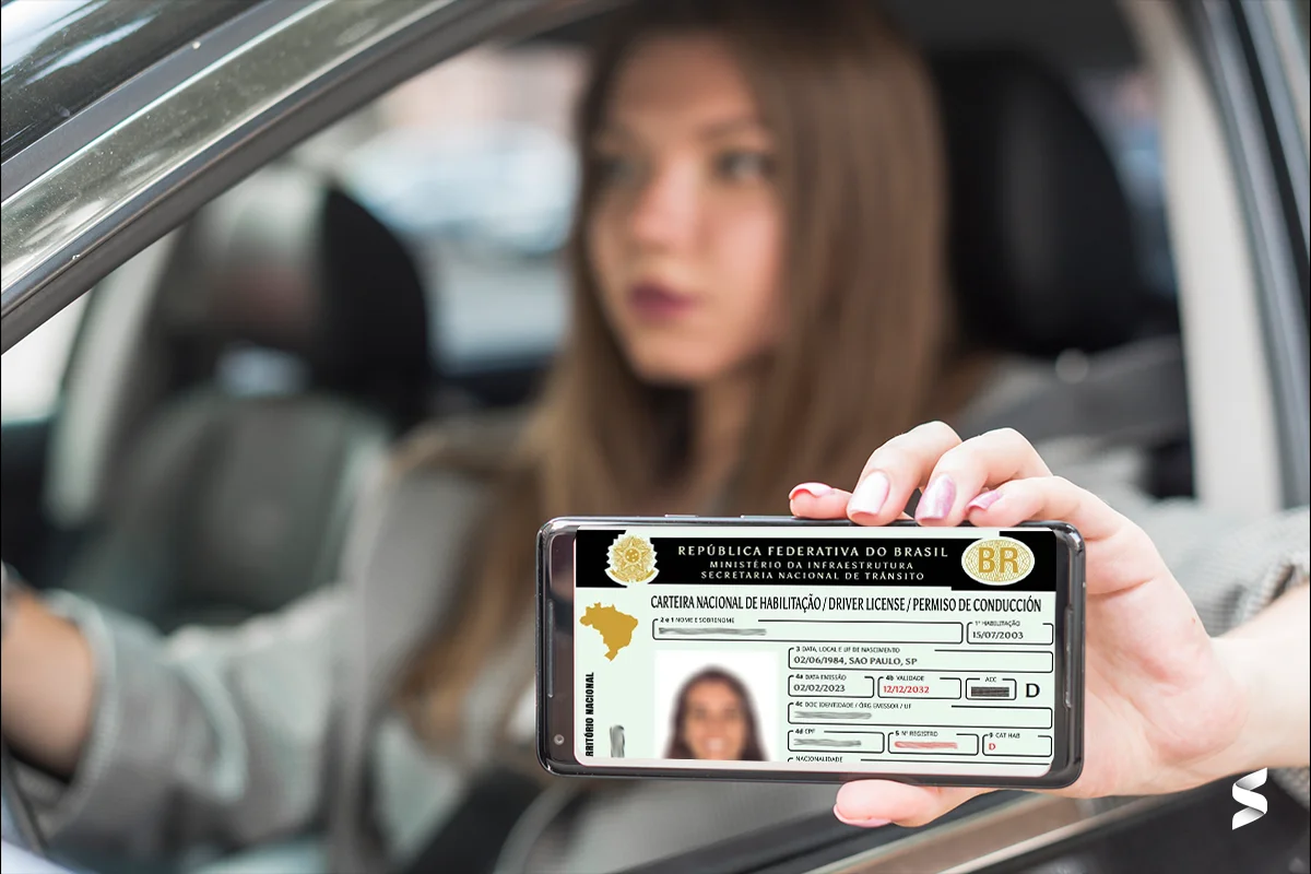 Mulher segurando a CNH digital no celular enquanto está dentro de um carro.