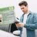 Homem com a CNH na mão e usando um celular, representando as mudanças no processo de habilitação em 2025.