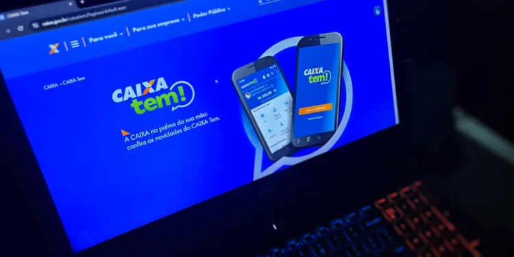 Tela do aplicativo CAIXA Tem exibida em um laptop, com interface mostrando saldo e funcionalidades do app
