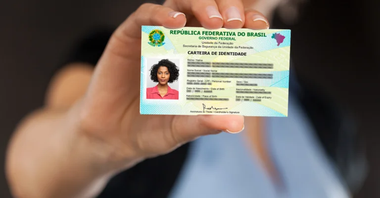 Carteira de identidade brasileira sendo segurada por uma mão, representando o processo de emissão.