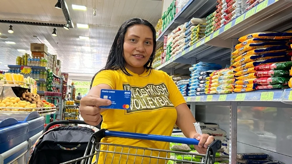 Mulher sorridente segurando cartão do programa Cartão Prato Cheio em supermercado
