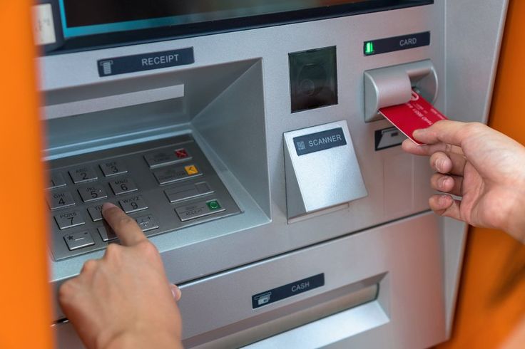 Pessoa inserindo cartão em caixa eletrônico enquanto digita a senha.