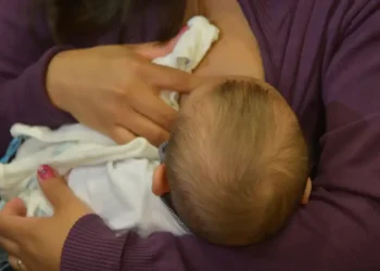 Imagem de uma mãe amamentando seu bebê, representando o vínculo entre a trabalhadora e o direito ao salário-maternidade.