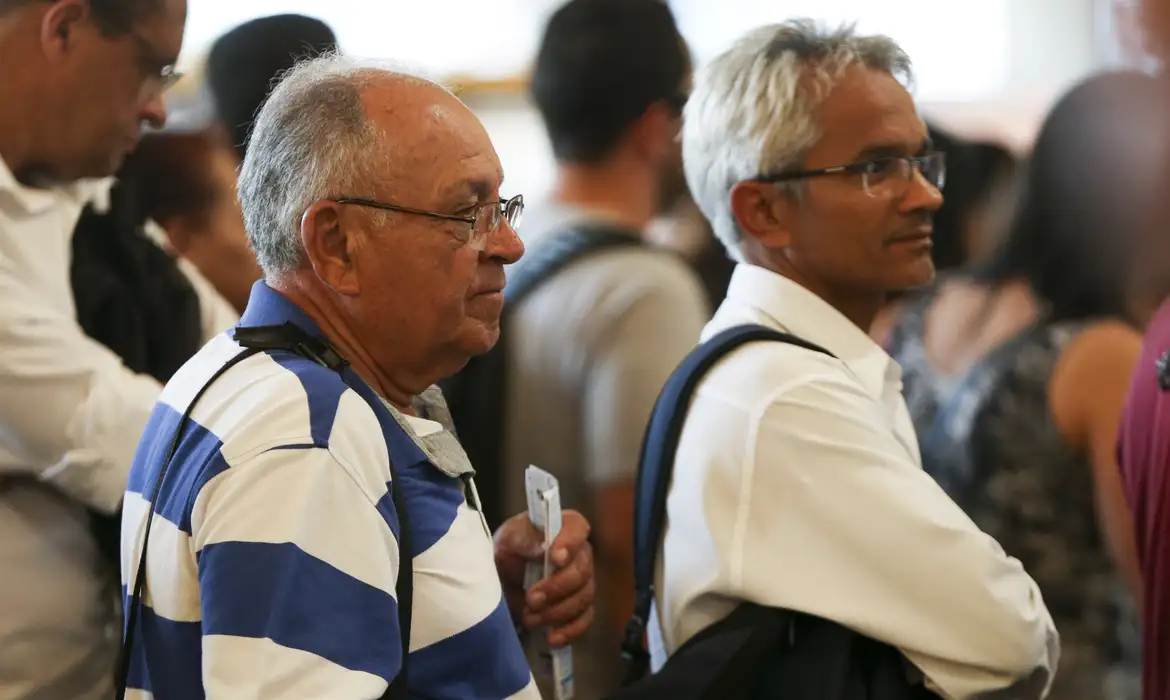 Homens idosos em uma fila de atendimento, aguardando para resolver questões relacionadas ao INSS.