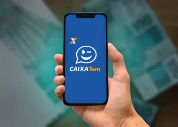 Logo do Caixa Tem exibido em um celular, com notas de 100 reais ao fundo.