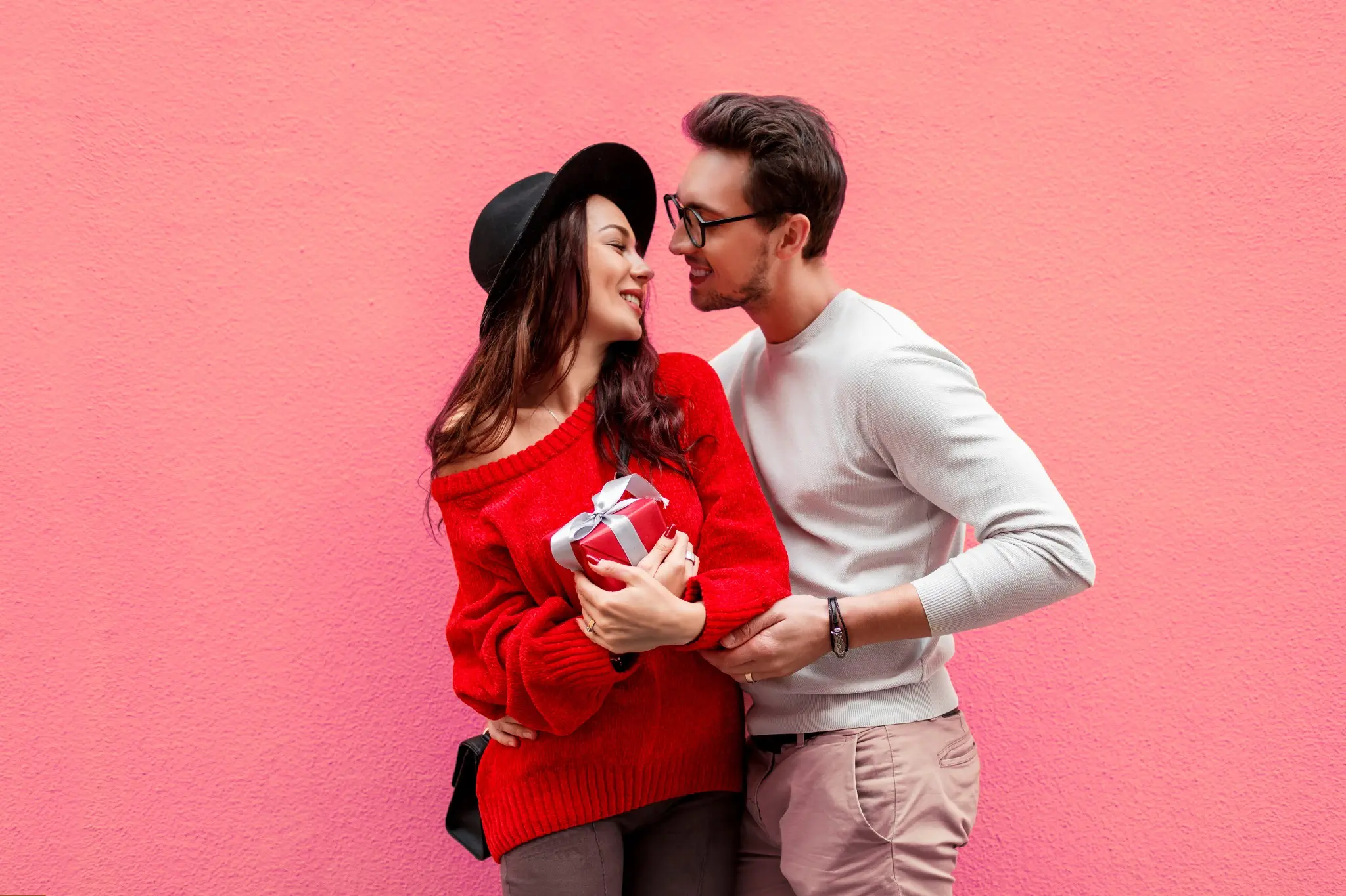 Casal sorridente e apaixonado posando diante de um fundo rosa, celebrando o 12 de junho.