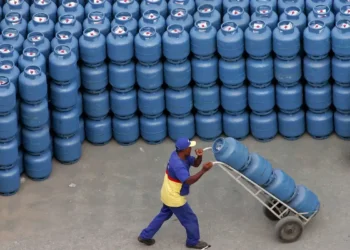 Trabalhador transportando botijões de gás empilhados em um carrinho.