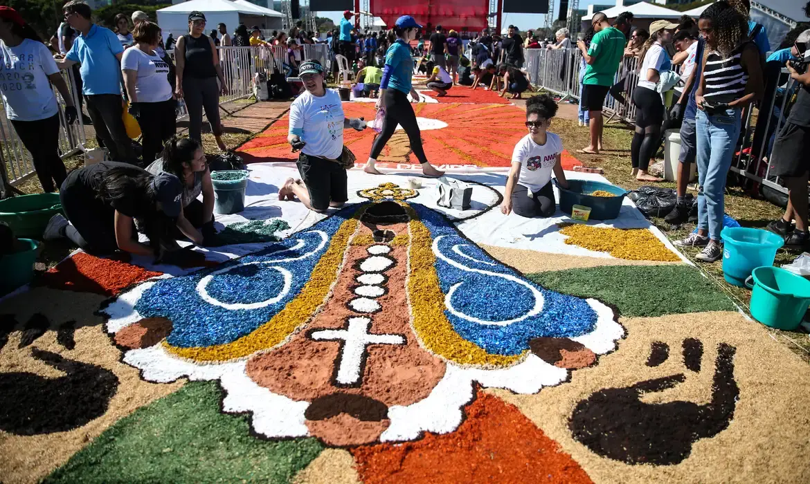 Grupo de pessoas criando um tapete de flores coloridas durante as festividades de Corpus Christi em uma capital brasileira.