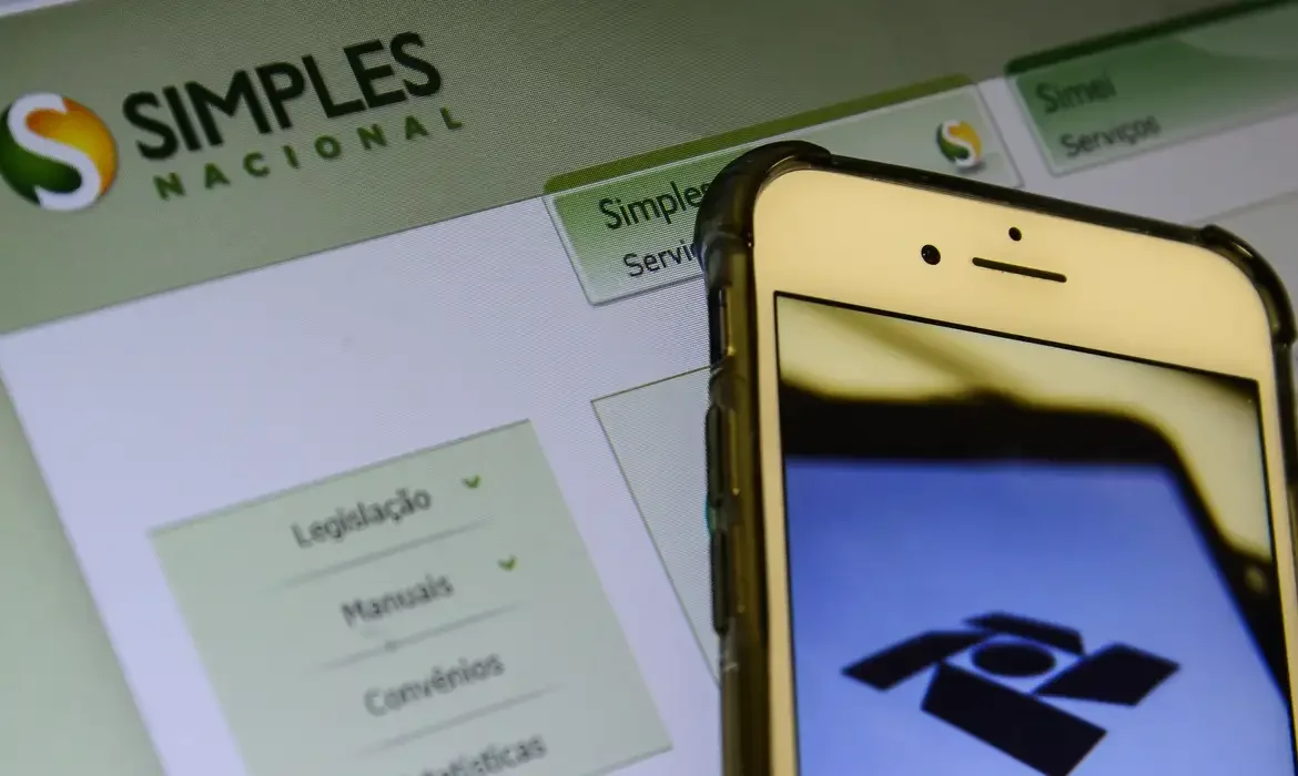 Tela do Simples Nacional em um computador e aplicativo da Receita Federal em um smartphone
