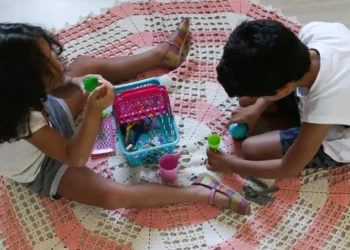 Crianças brincando no chão com brinquedos de Play-Doh em ambiente doméstico.