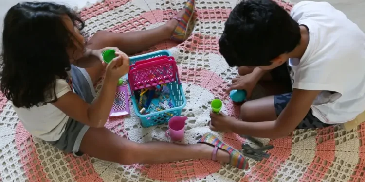 Crianças brincando no chão com brinquedos de Play-Doh em ambiente doméstico.
