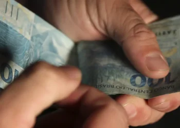 Pessoa contando notas de 100 reais com as mãos