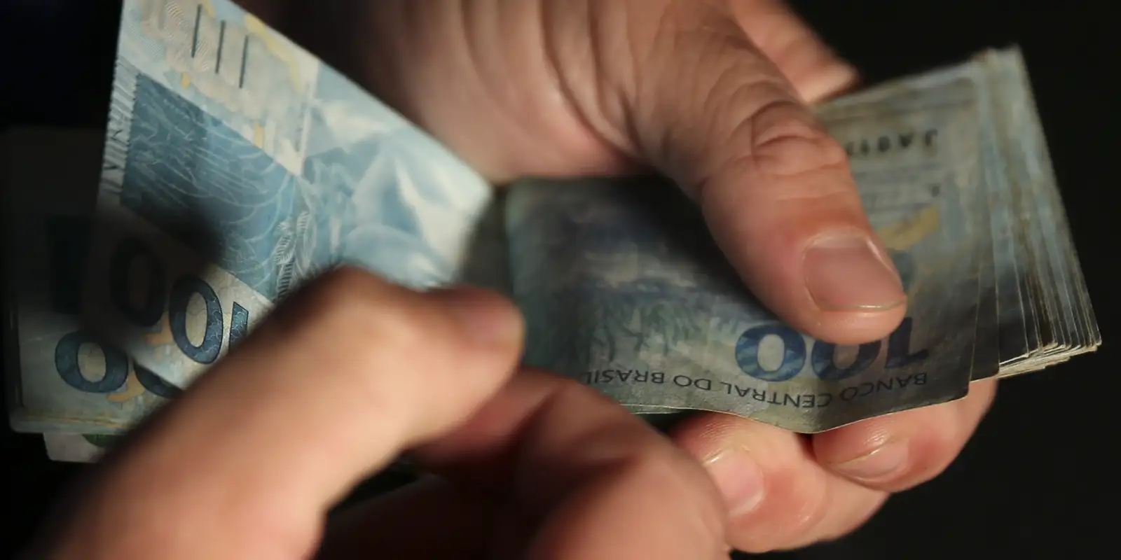 Pessoa contando notas de 100 reais com as mãos