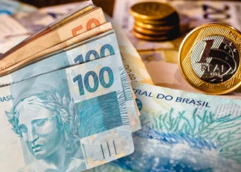 Notas de 100 reais e moedas do Real, ilustrando o conceito de finanças e dinheiro no Brasil.