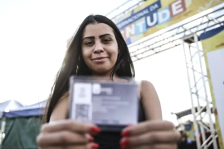 Jovem segurando cartão do ID Jovem durante evento público