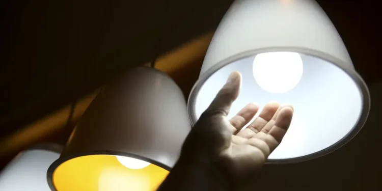 Mão alcançando lâmpada acesa, representando os benefícios de tarifas de energia elétrica reduzidas.