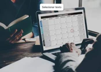 Pessoa utilizando calendário online no notebook enquanto outra lê um livro