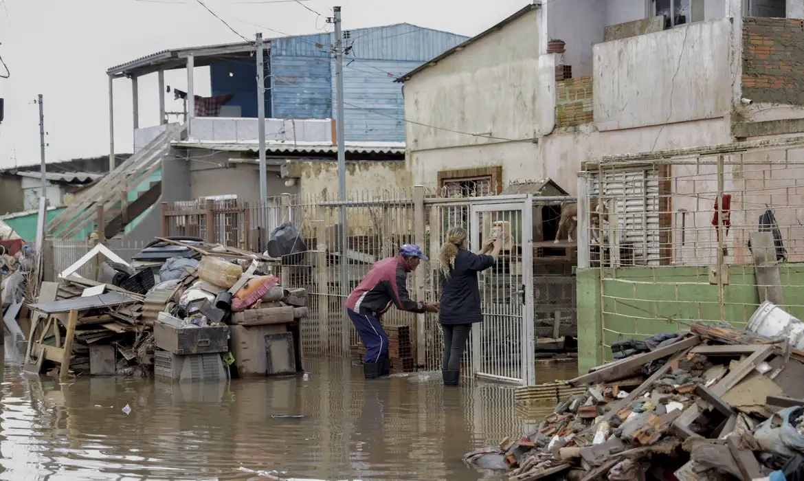 Pessoas tentando proteger suas casas durante enchente causada por fortes chuvas.