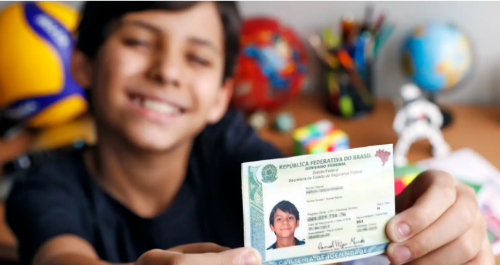 Menino sorrindo e segurando o novo RG modelo digital, com a descrição de como fazer a troca do documento.
