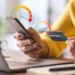 Pessoa consultando score de crédito pelo celular com cartão na mão