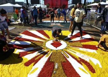 Pessoas confeccionando um tapete colorido de flores para celebração religiosa durante o feriado de Corpus Christi.