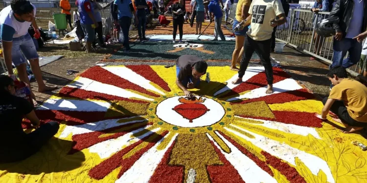 Pessoas confeccionando um tapete colorido de flores para celebração religiosa durante o feriado de Corpus Christi.