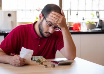 Homem preocupado analisando contas, dinheiro e calculadora