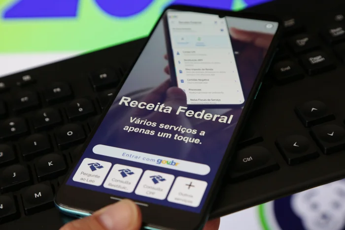 Imagem de um celular exibindo a página da Receita Federal, com opções para consulta de serviços, incluindo consulta de restituição do Imposto de Renda.