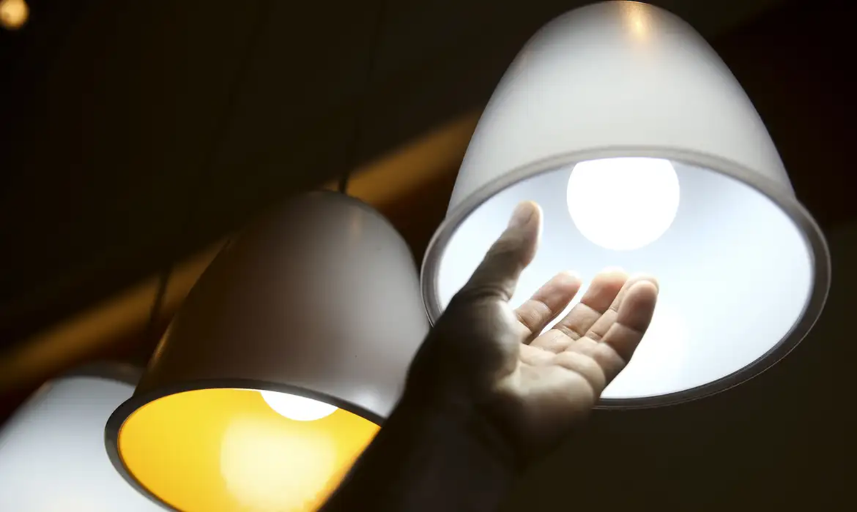 Pessoa alcançando uma lâmpada, simbolizando o impacto do aumento na conta de luz e a busca por soluções.