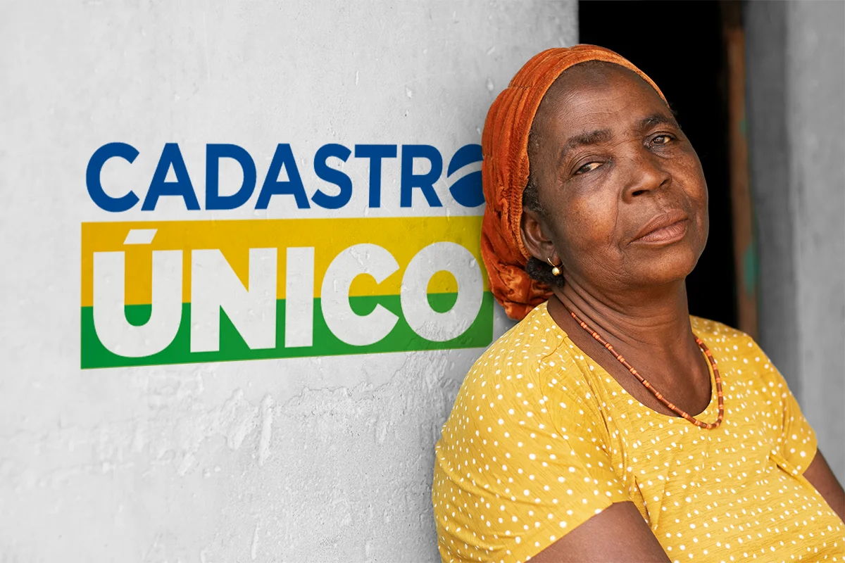 Mulher idosa em frente a uma parede com o logo do Cadastro Único, representando o acesso a benefícios sociais.