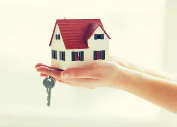 Mão segurando uma casa em miniatura com uma chave, representando o Aluguel Social.