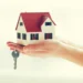 Mão segurando uma casa em miniatura com uma chave, representando o Aluguel Social.