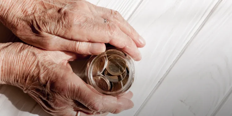 Mãos idosas segurando pote com moedas sobre mesa de madeira