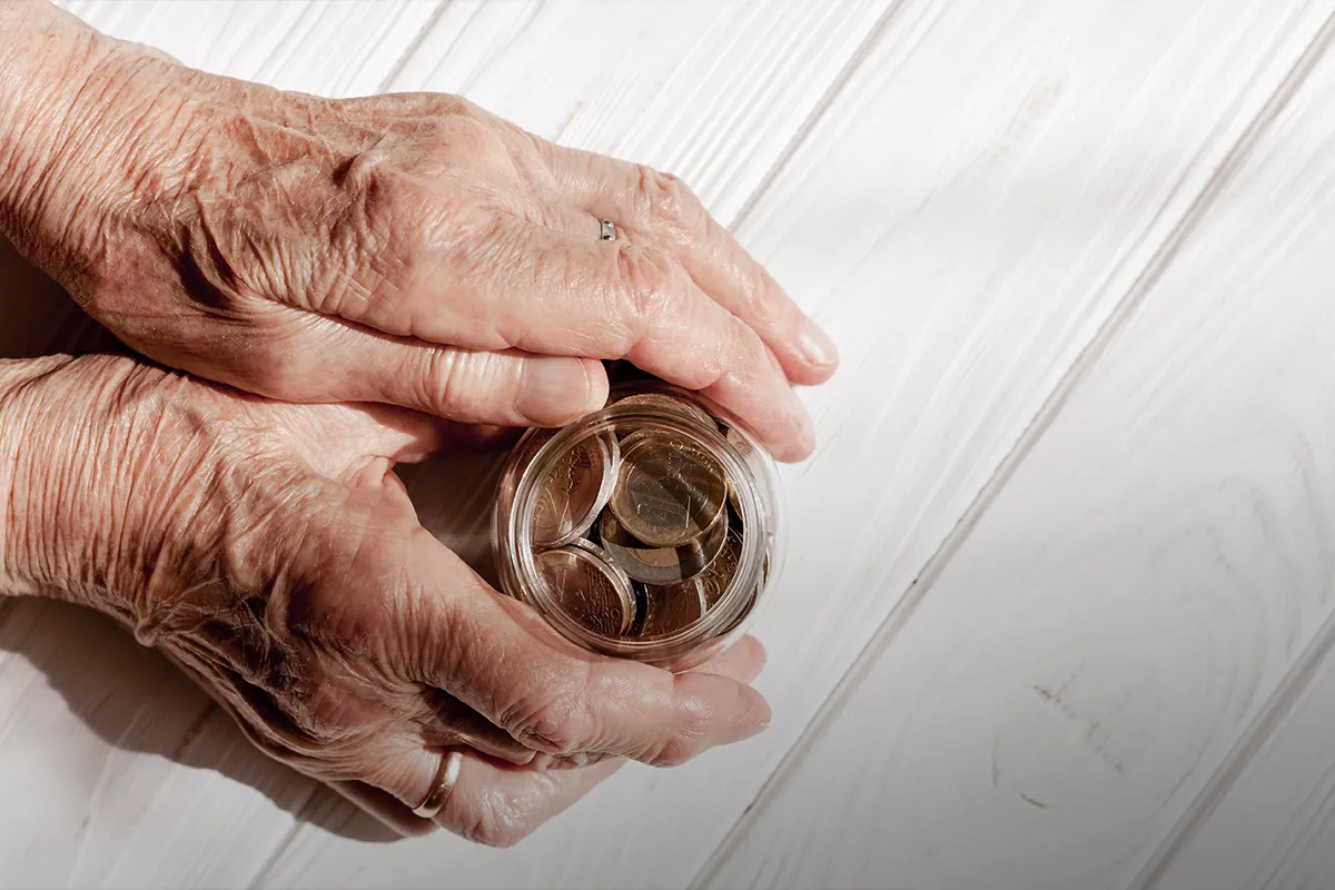 Mãos idosas segurando pote com moedas sobre mesa de madeira