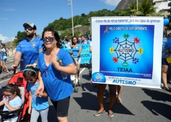 Imagem de evento de conscientização sobre autismo, com pessoas participando de uma caminhada com cartazes e roupas azuis, celebrando o Dia Mundial de Conscientização do Autismo.