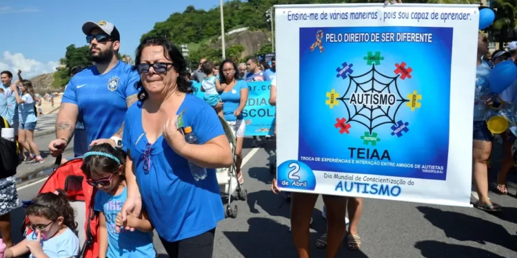 Imagem de evento de conscientização sobre autismo, com pessoas participando de uma caminhada com cartazes e roupas azuis, celebrando o Dia Mundial de Conscientização do Autismo.