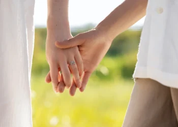 Casal de mãos dadas ao entardecer com anel de noivado visível, simbolizando o amor e união.