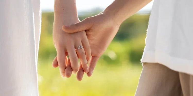 Casal de mãos dadas ao entardecer com anel de noivado visível, simbolizando o amor e união.